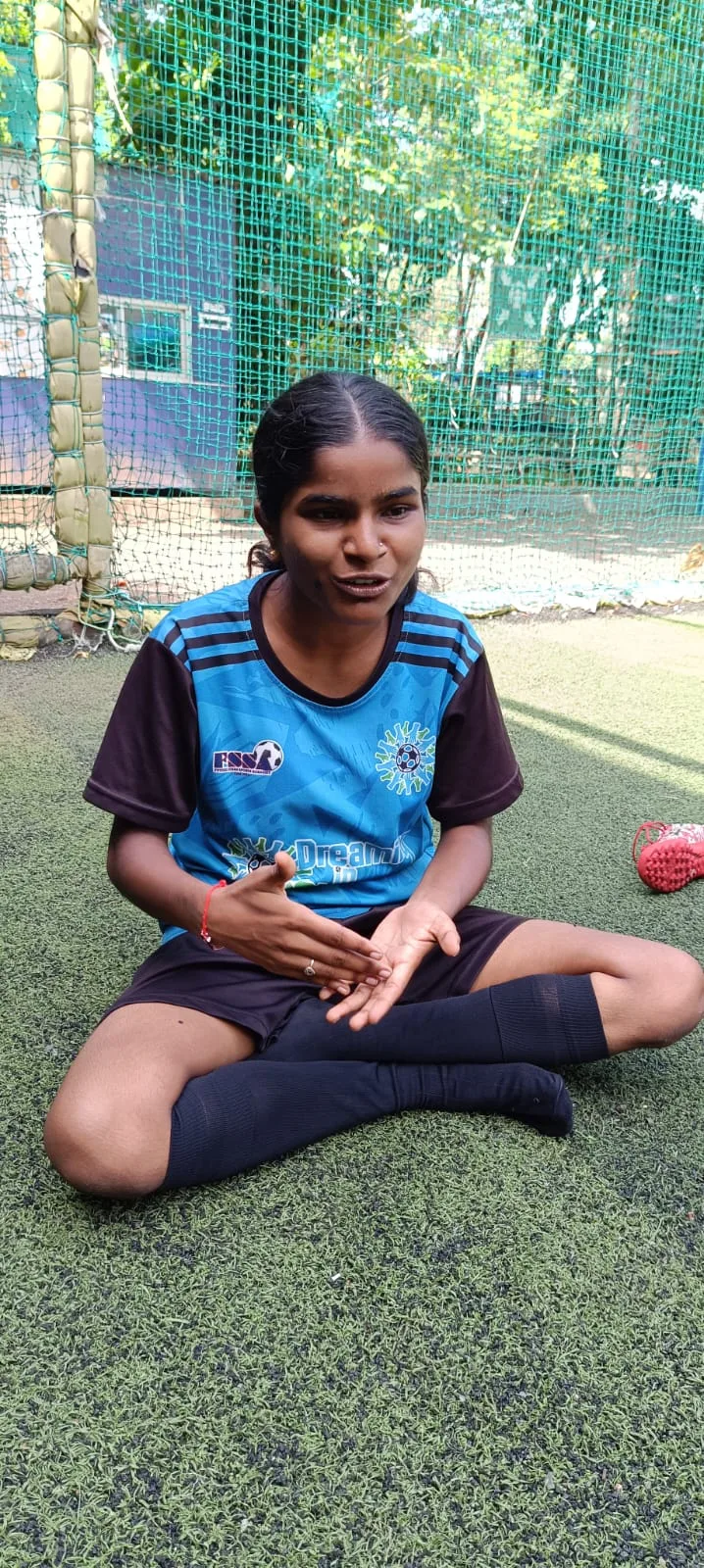 Nisha Athawale sitting on the pitch in her Dreaming In Slums kit